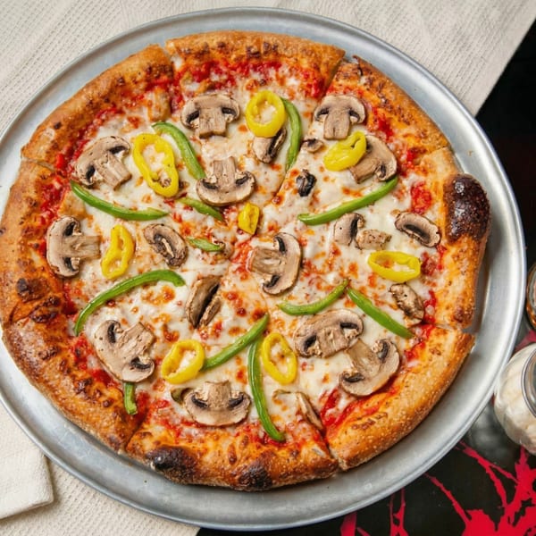 A whole pizza with mushrooms, green peppers, and banana peppers on a metal tray.