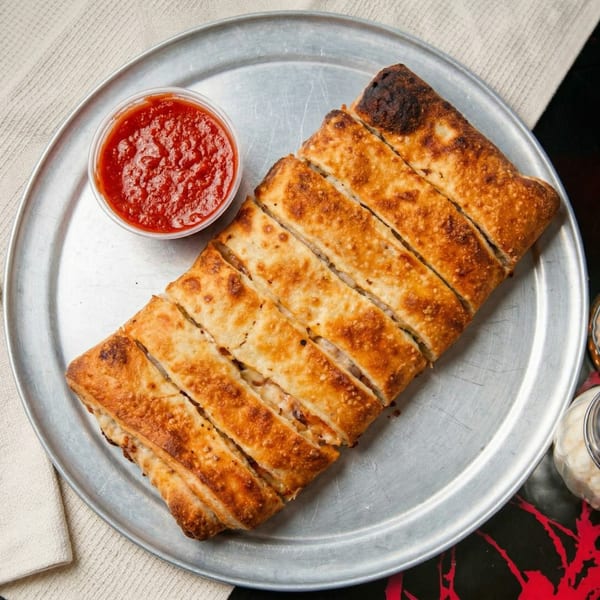 Golden-brown, sliced stromboli with a side of red marinara sauce on a metal pizza tray.
