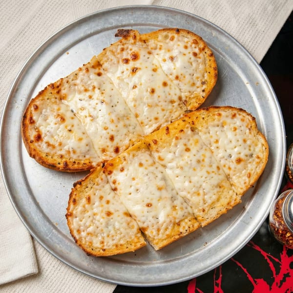 Two golden-brown cheese bread slices, topped with melted mozzarella, on a round metal tray.