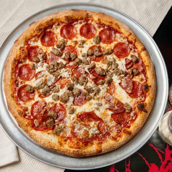 A whole pepperoni, sausage, and ham pizza on a metal tray, with a white napkin and red table.