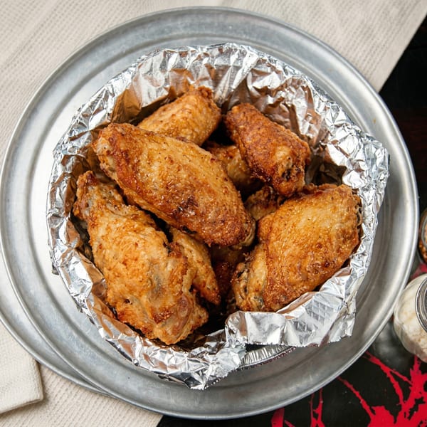 Crispy fried chicken wings in a foil-lined metal bowl on a silver tray.