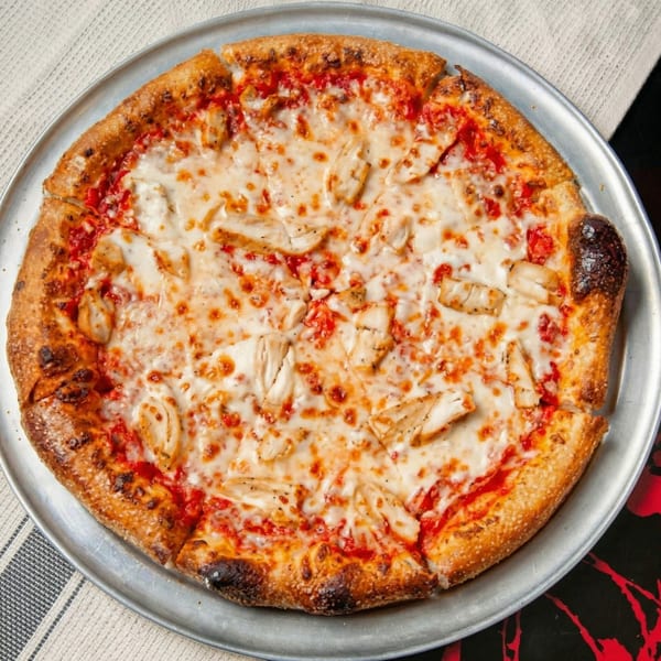 A whole chicken pizza with melted cheese and red sauce on a metal tray.