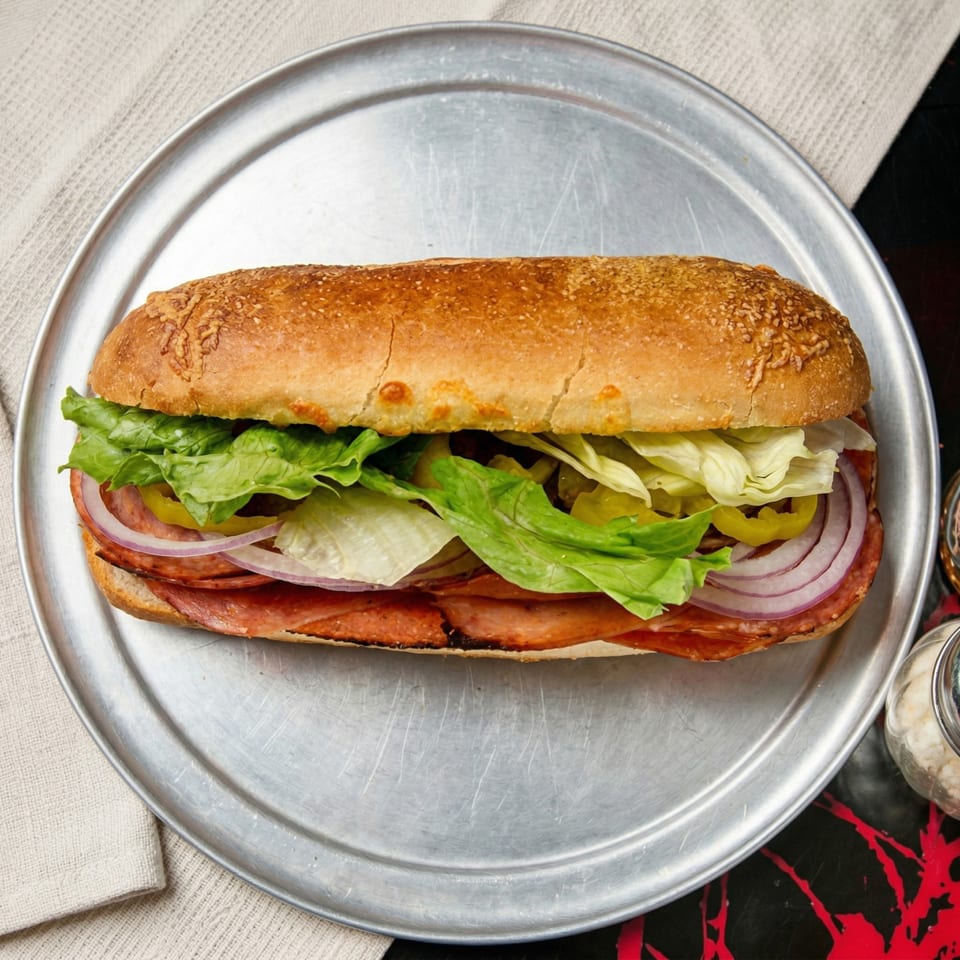 A large deli sandwich with lettuce, onions, and meat on a metal tray.