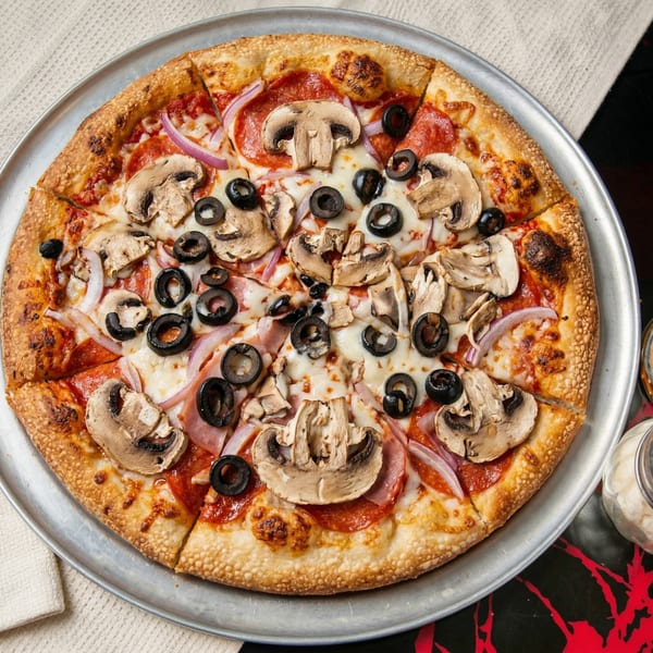 A whole pepperoni pizza with mushrooms, black olives, and red onions on a metal tray.
