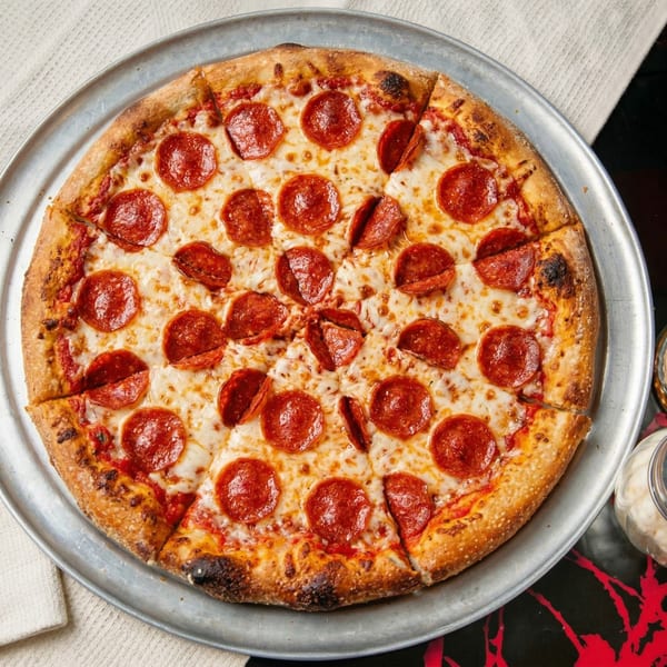 A whole pepperoni pizza, sliced, on a metal tray with a white napkin and red-patterned table.